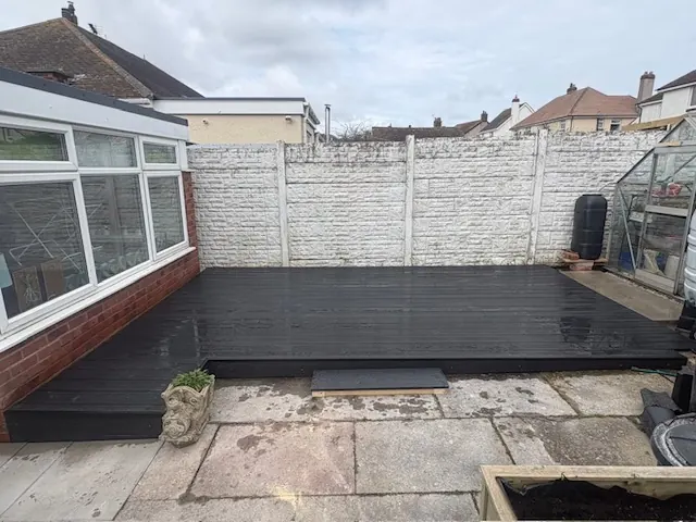 Dark composite decking laid at the back of a house beside a conservatory. One of our jobs.