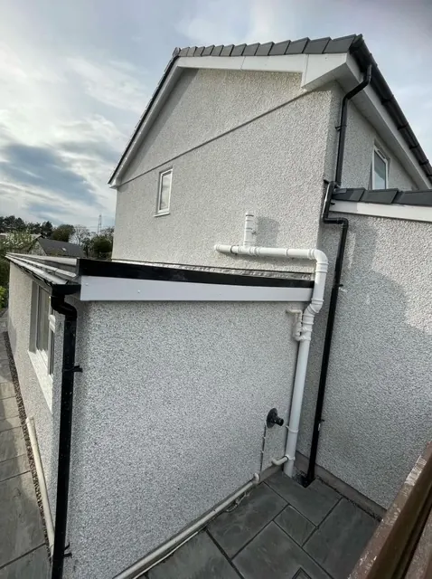 Freshly rendered gable end and side wall of a house, with new white downpipes. One of our jobs.